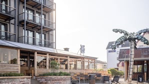 A modern building with a pool area, including a lounge with outdoor seating and a palm tree decoration. - Bretterbude Büsum (Büsum)