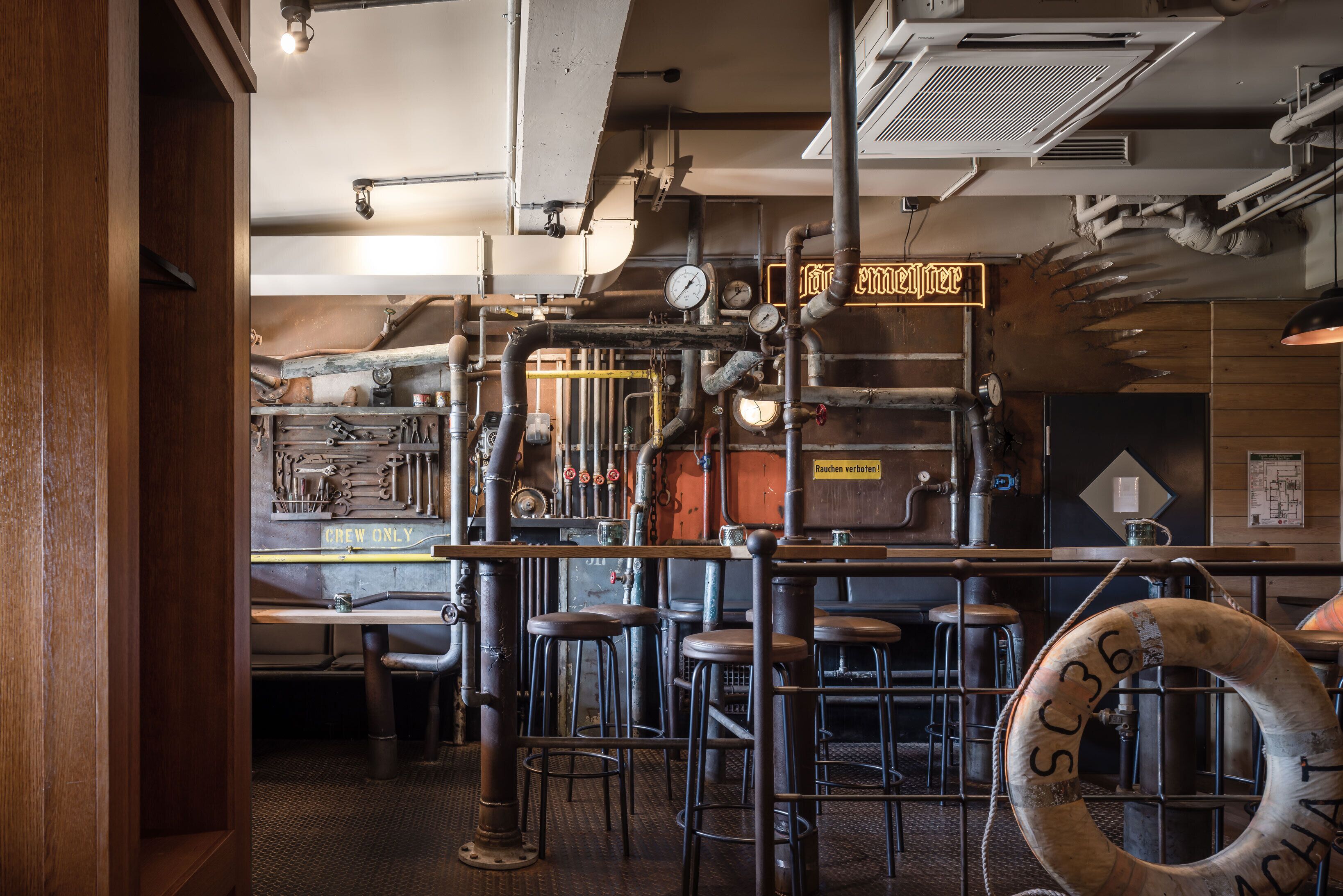 A bar area with stools, a bar counter, and a neon sign.