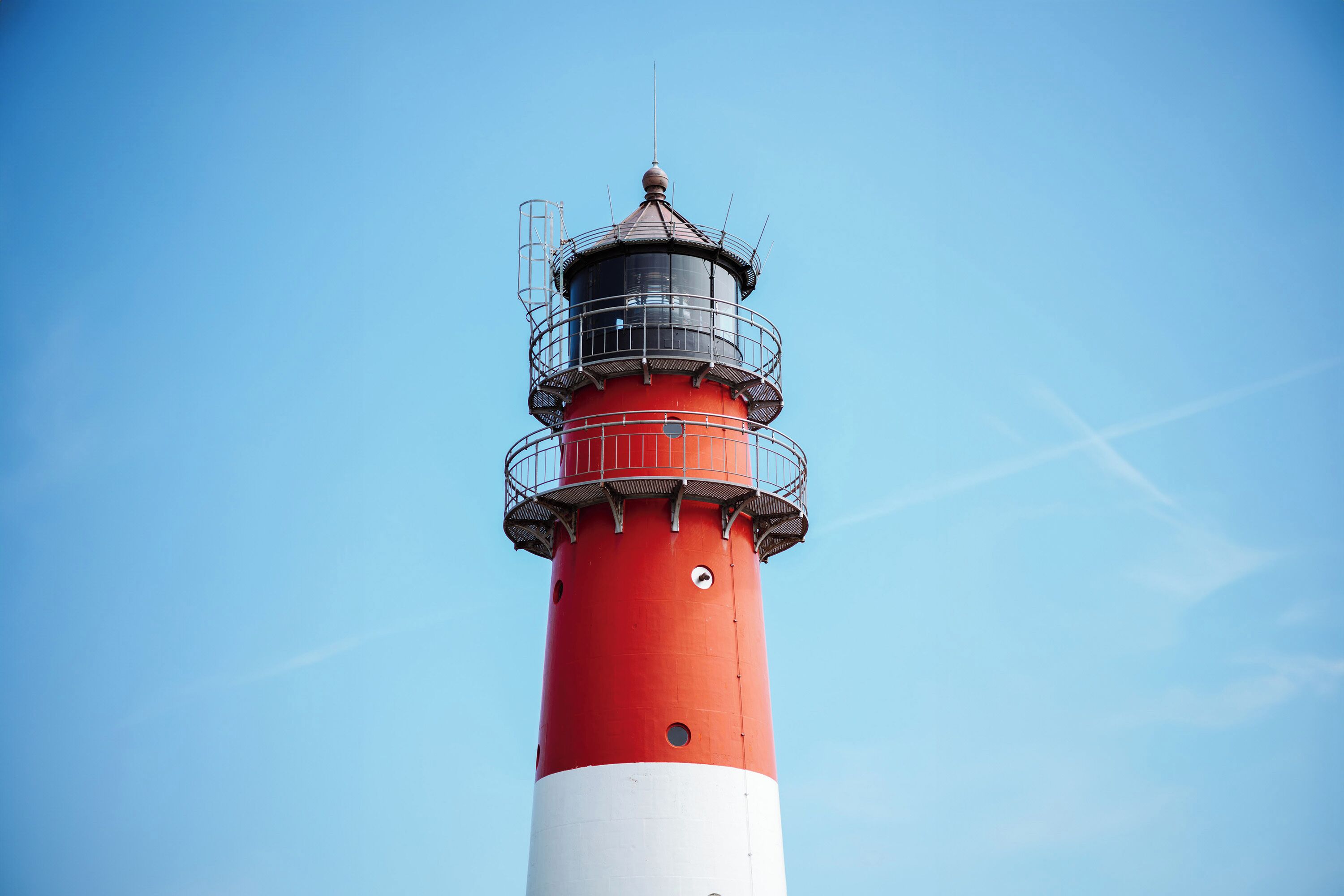 Un faro con una estructura cilíndrica roja y blanca, bajo un cielo azul despejado.