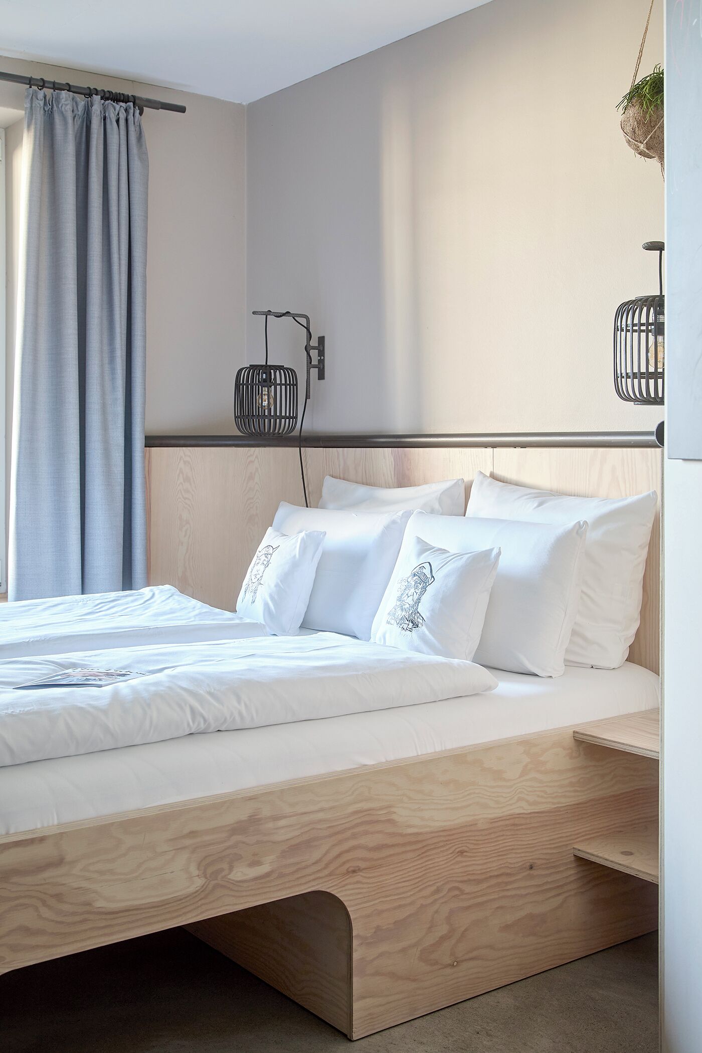 Une chambre moderne avec un cadre de lit en bois, du linge de lit blanc et une plante suspendue.