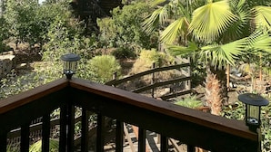 Una terraza de madera con barandilla, rodeada de exuberante vegetación y un paisaje de montañas.