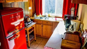 Una cocina compacta con gabinetes de madera, un refrigerador rojo y una ventana con cortinas rojas.