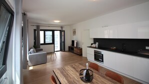 A modern kitchen with white cabinets, a black countertop, and a wooden dining table. - Boutique Apartment 9 (Lugano)