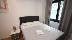 A neatly made bed with white linens, a bedside table with a lamp, and a window with curtains. - Boutique Apartment 9 (Lugano)
