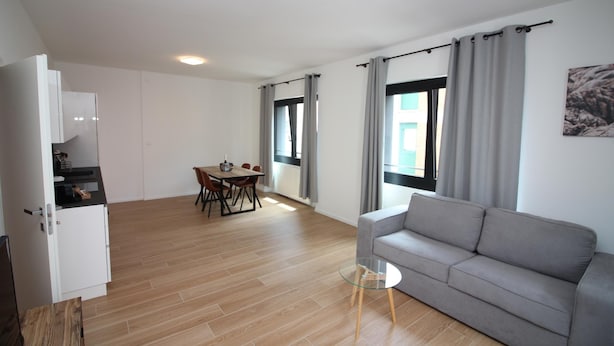 A modern living room with a grey sofa, a glass coffee table, and a dining area with a table and chairs. - Boutique Apartment 9 (Lugano)