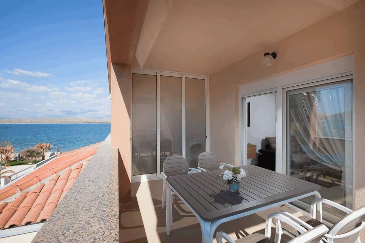 A balcony with a table and chairs, a view of the sea, and a sliding glass door.