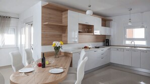 Una cocina moderna con armarios blancos, una mesa de comedor de madera y un ventanal que proporciona luz natural.
