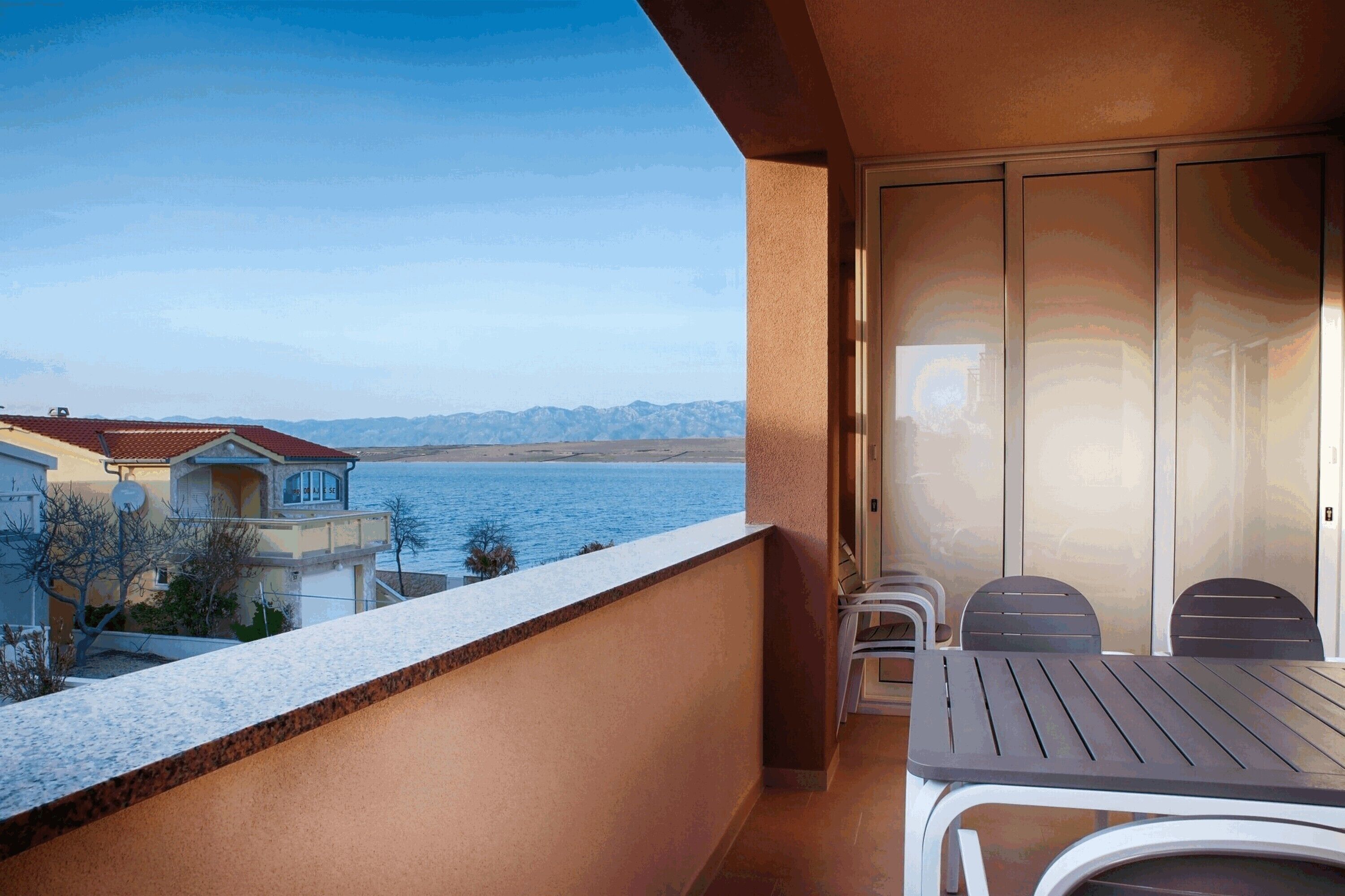 A balcony with a table and chairs, overlooking a body of water and distant mountains.