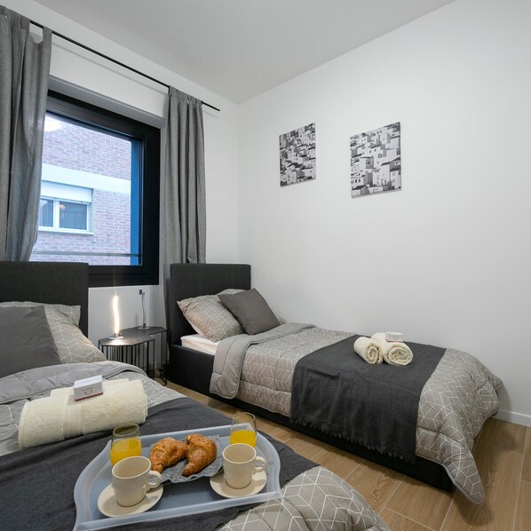 A modern bedroom with two beds, a window with curtains, and artwork on the wall.