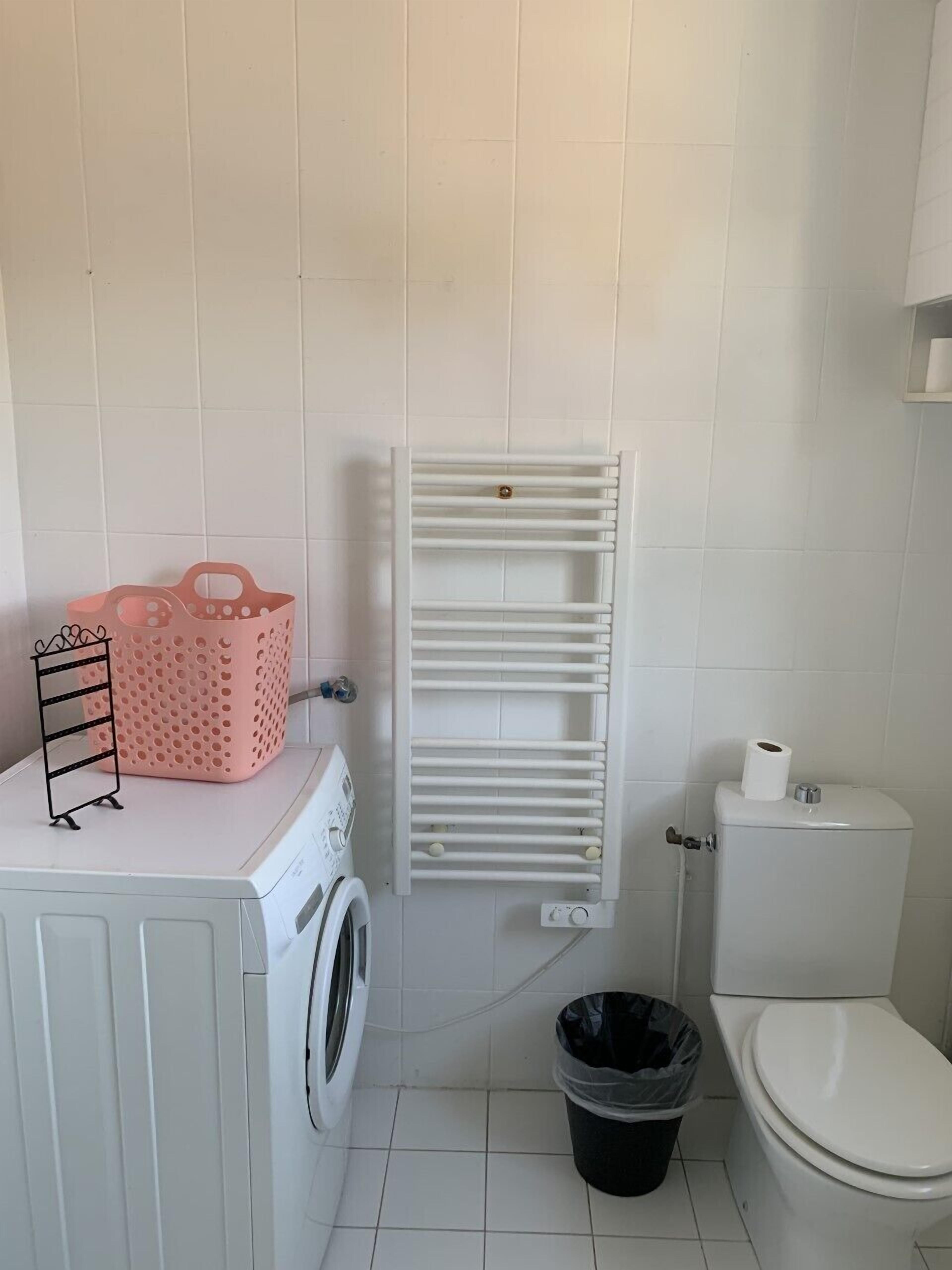 Une petite salle de bain équipée d’un lave-linge, de toilettes et d’un radiateur blanc.