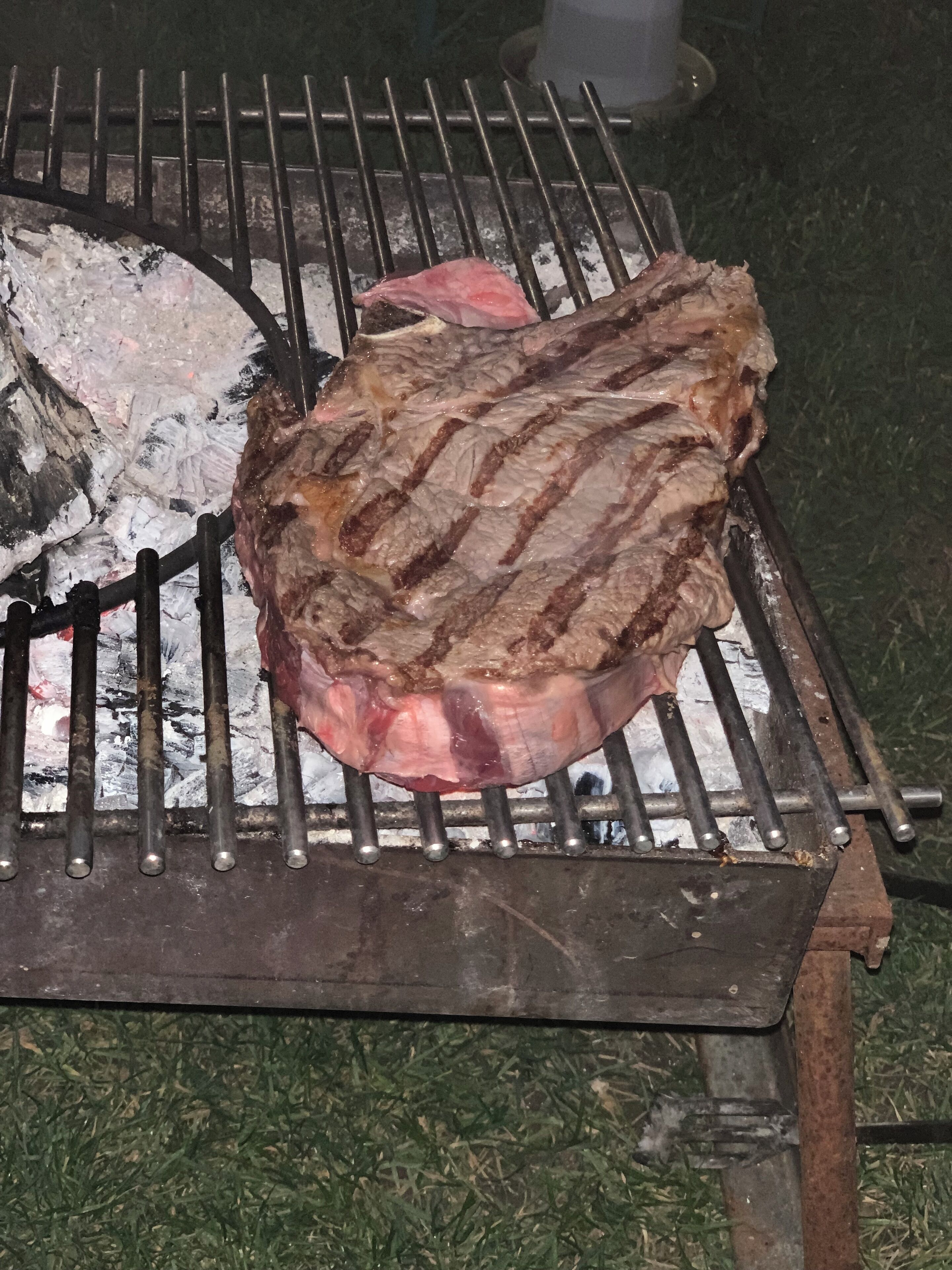 A steak being grilled on a metal grate over charcoal.