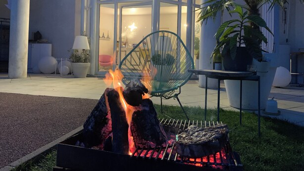 A modern outdoor seating area with a fire pit, a green chair, and a potted plant. - Casabina (Chelles)