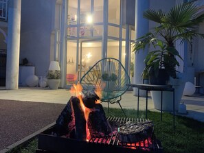 Un espacio exterior moderno con zona de estar, un brasero, una silla verde y una planta en maceta.