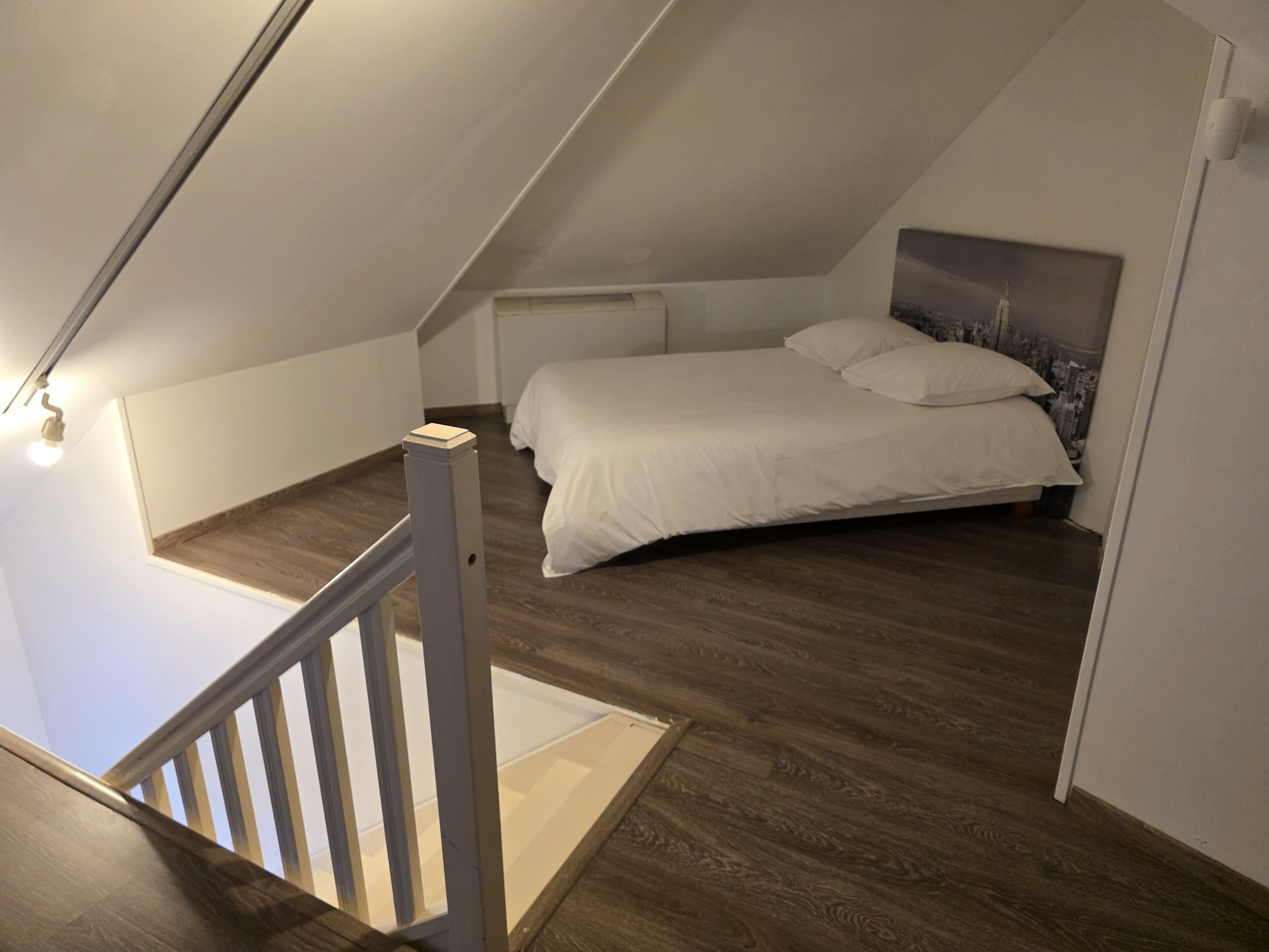 A bedroom with a sloped ceiling, a bed with white bedding, and a wooden floor.