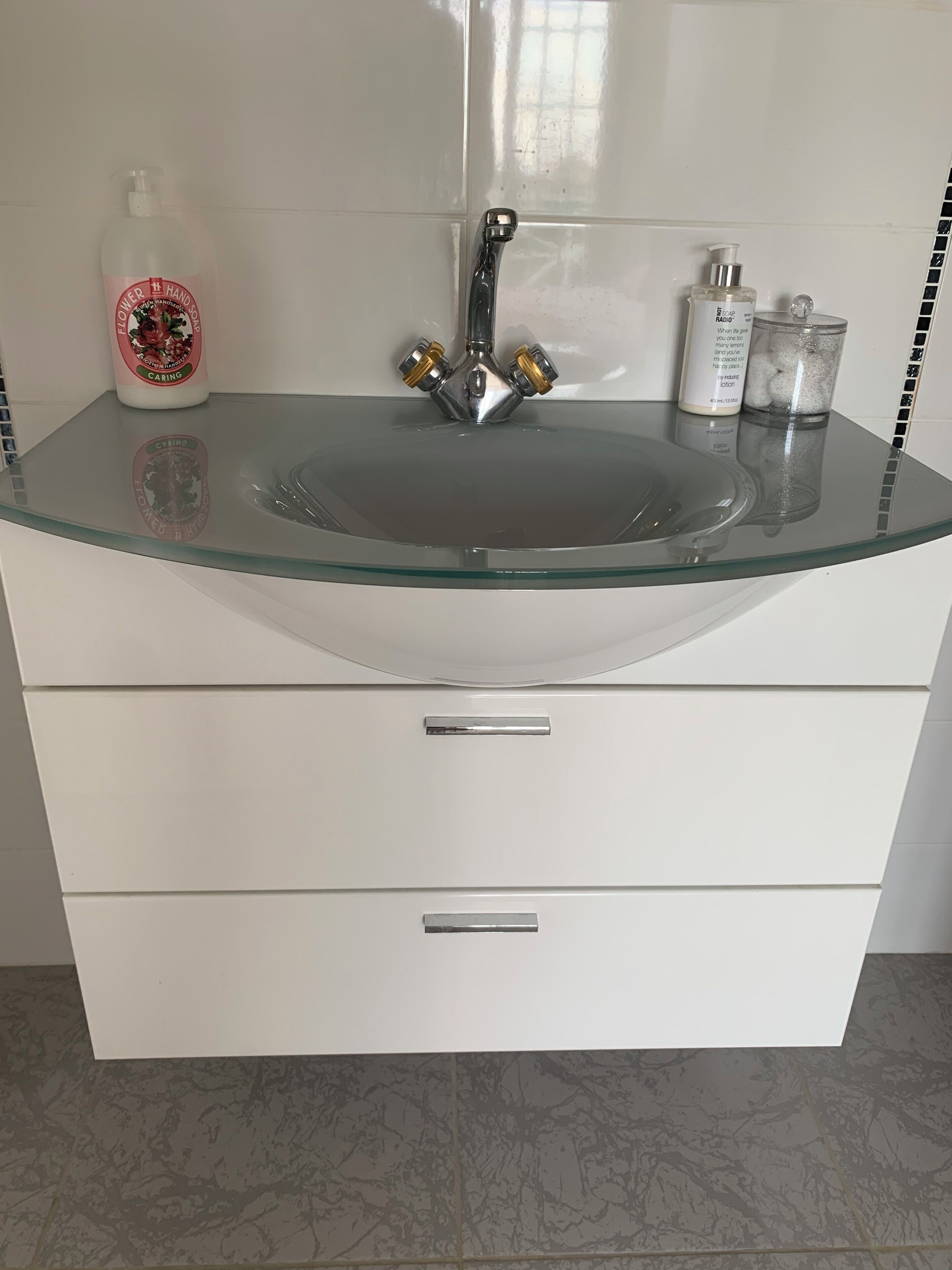 A bathroom with a glass sink, a faucet, and toiletries on the countertop.