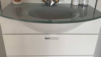 A bathroom with a glass sink, a faucet, and toiletries on the countertop.