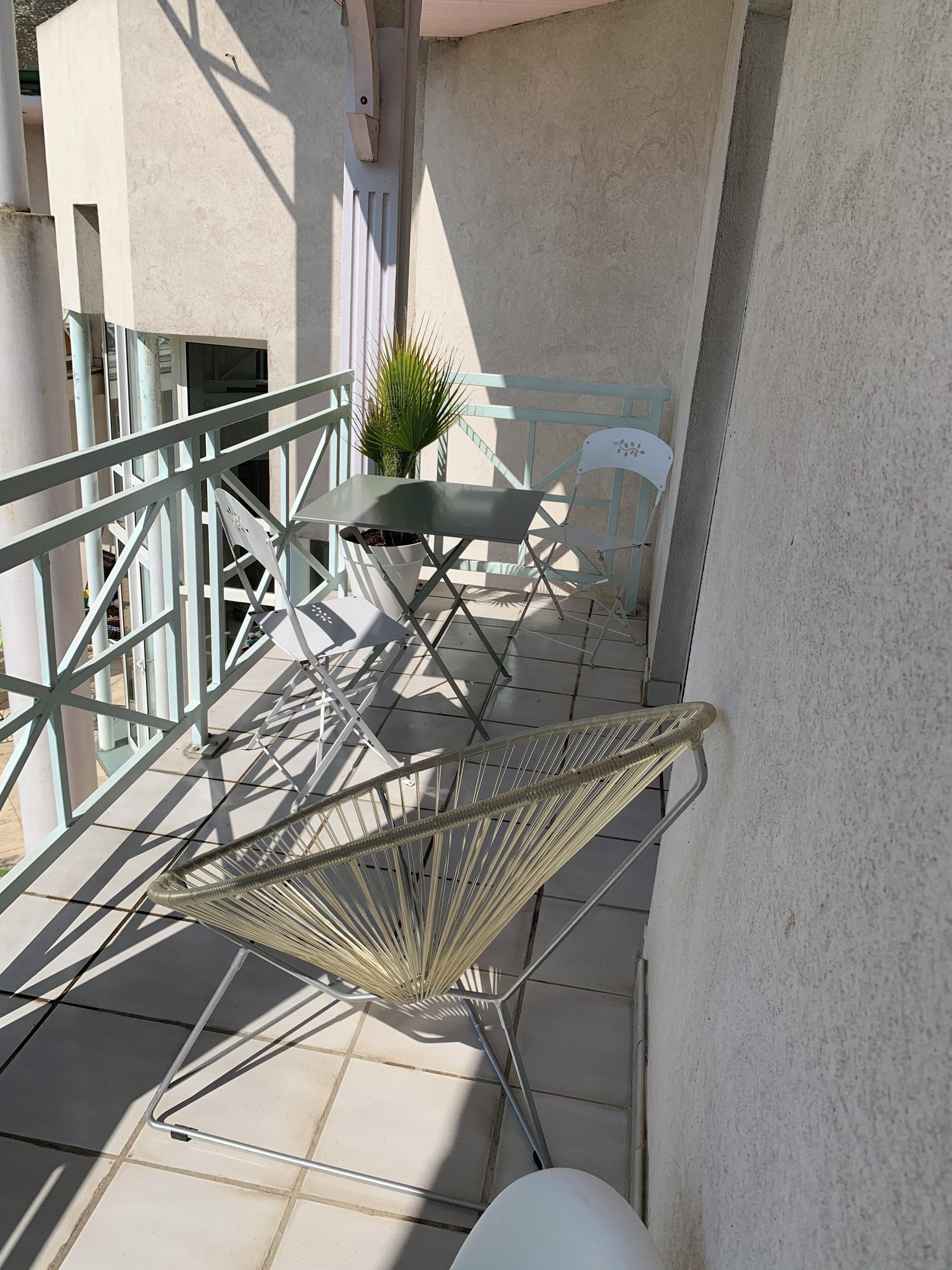 Een balkon met een metalen stoel, een kleine tafel met een bloempot en een witte stoel.