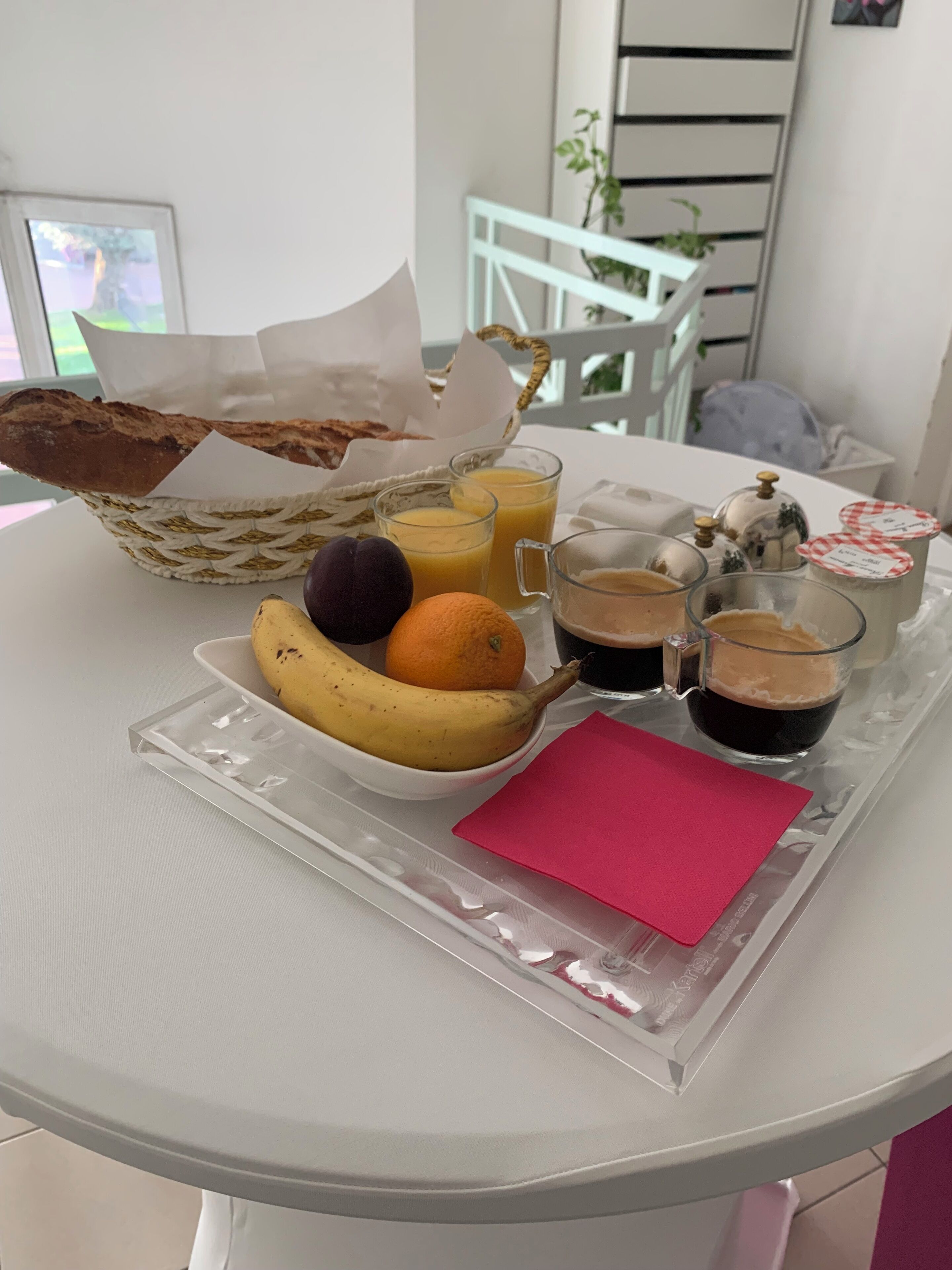 A breakfast tray with bread, fruits, and beverages on a white table.