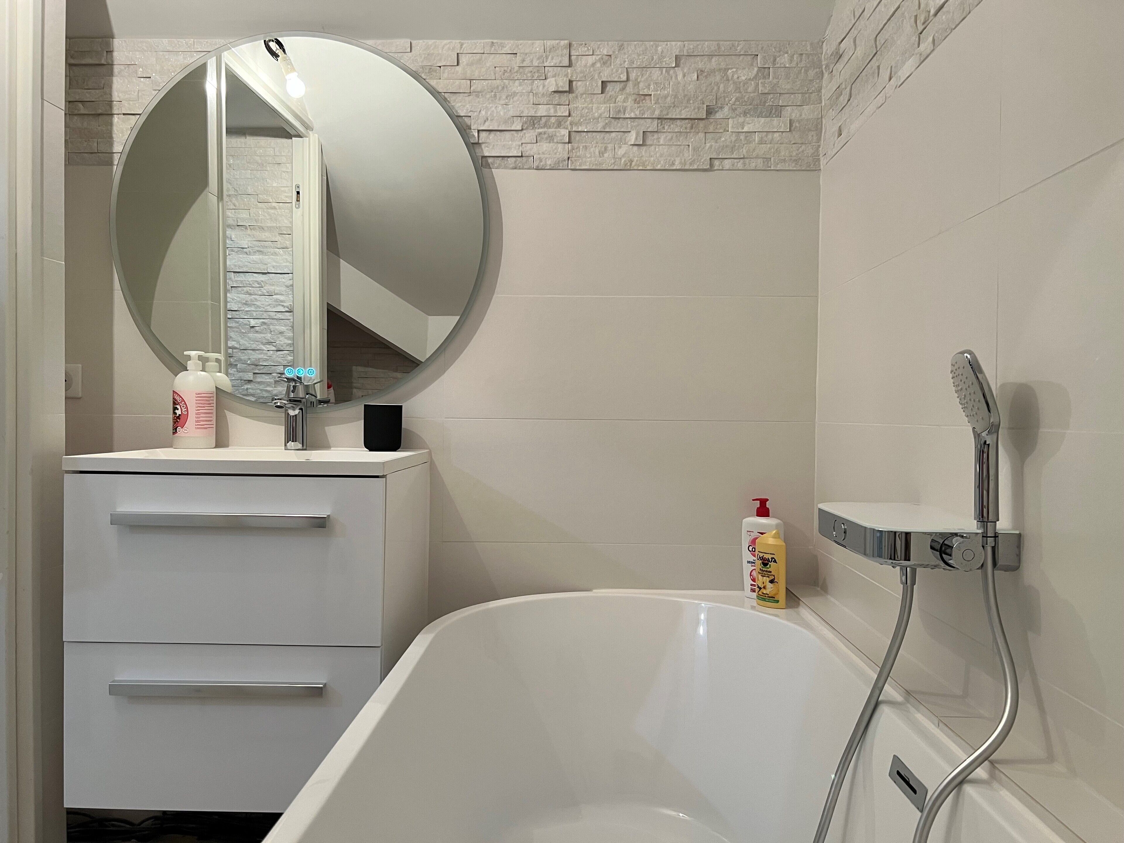 Un baño moderno con una bañera blanca, un espejo redondo y un cabezal de ducha.