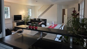 A modern living room with a black leather sofa, a dining table with red vases, and a staircase leading to an upper floor. - Casabina (Chelles)