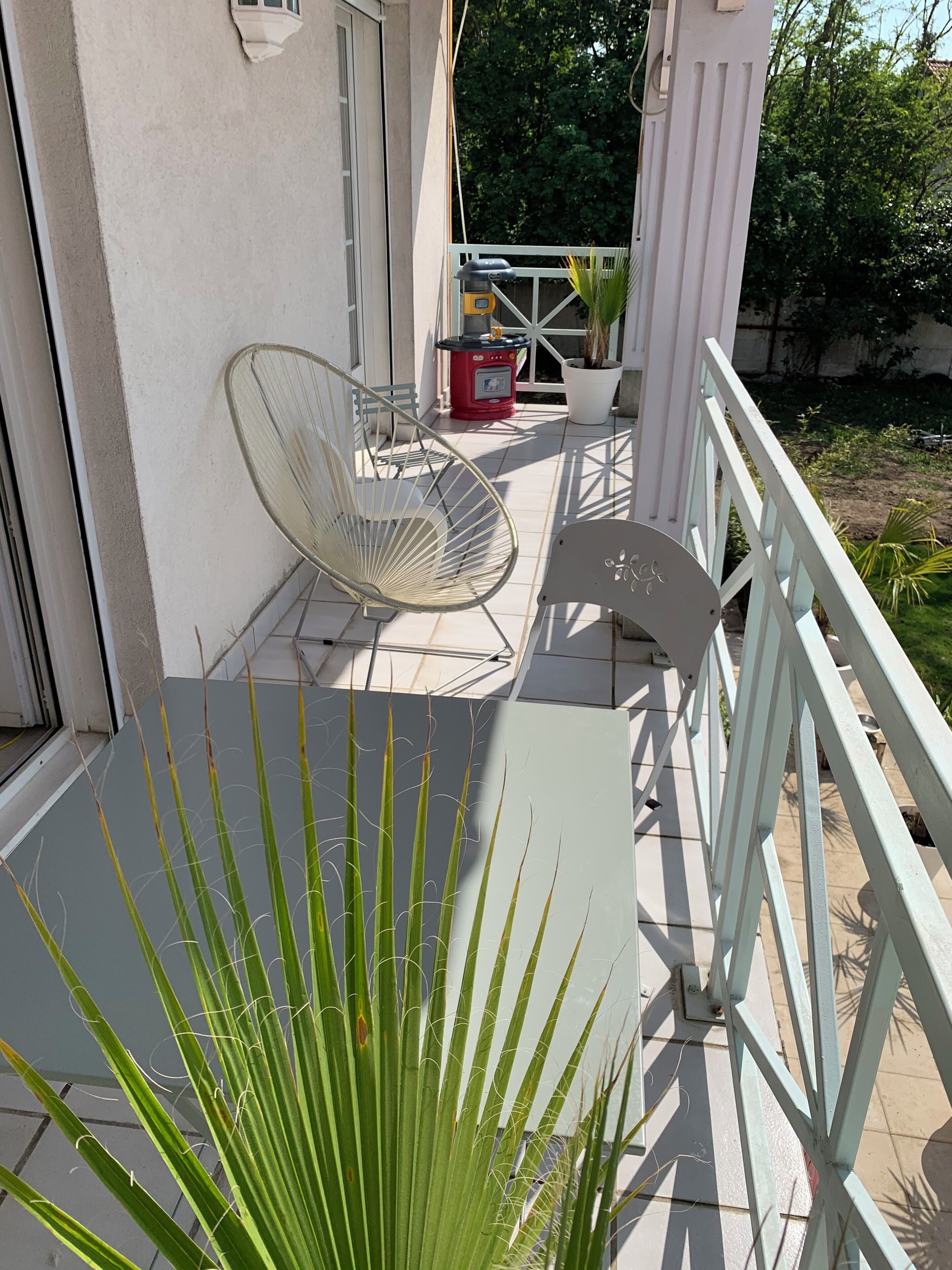 Een balkon met een witte stoel, een tafeltje en een bloempot.