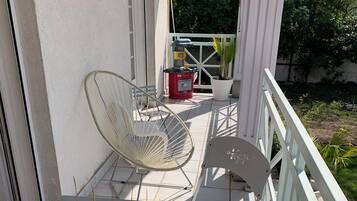 Een balkon met een witte stoel, een tafeltje en een bloempot.