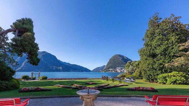 Un jardin agrémenté d’une fontaine, de bancs et offrant une vue sur les montagnes et un lac.