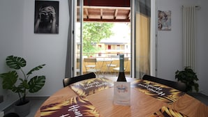 Un coin repas avec une table en bois, des chaises et une bouteille de champagne. De chaque côté de la table, on trouve des plantes en pot.