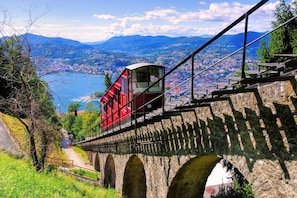 A cable car moving over a stone bridge with a city and mountains in the background. - Casa Rosa in Lugano With 2 Bedrooms and 1 Bathrooms (Lugano)