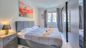 Une chambre moderne avec un grand lit, des tables de chevet, une commode, une fenêtre avec des rideaux et un tableau au mur.
