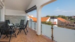 A balcony with a table and chairs, a stone wall, and a view of houses. - Apartment Wenig (Vir)
