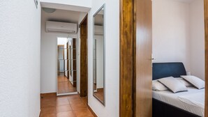 A narrow hallway with a tiled floor, leading to a bedroom with a bed and a large mirror. - Apartment Wenig (Vir)