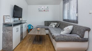 A compact living space with a grey sofa, a small wooden table, a TV on a cabinet, and a wall with framed pictures. - Apartment Wenig (Vir)