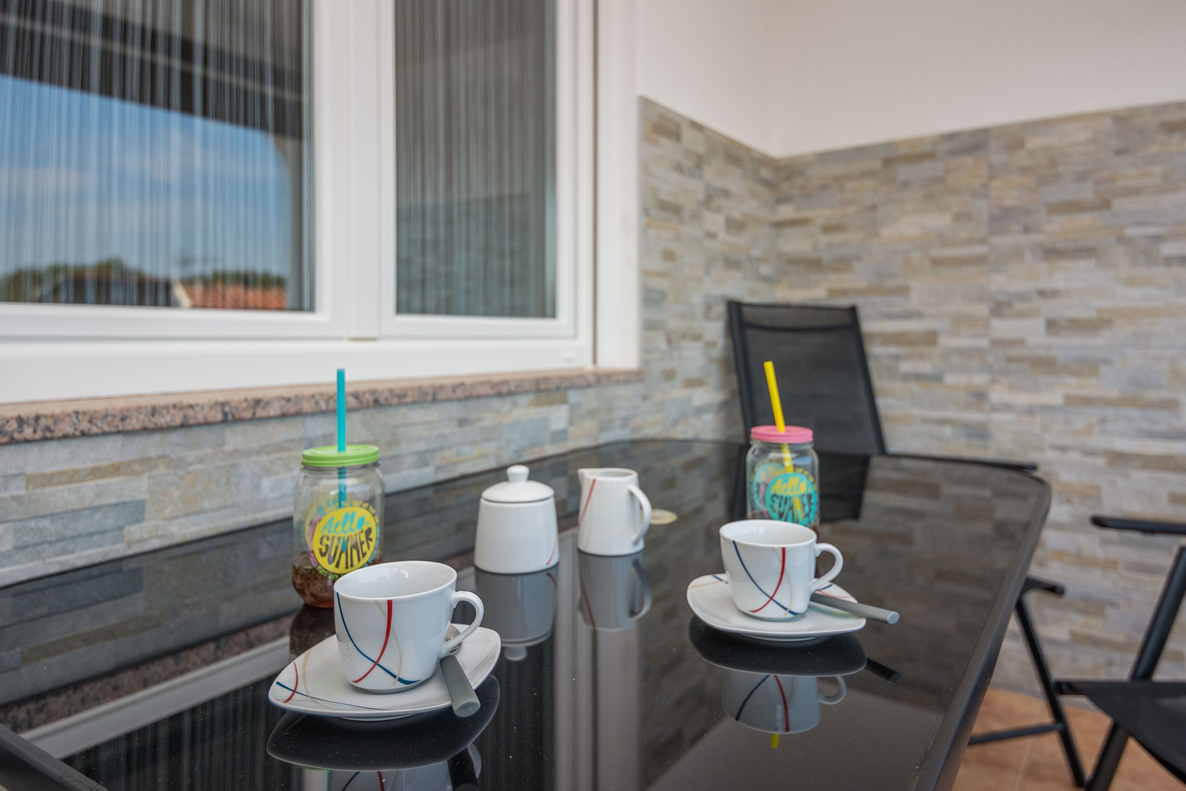 A glass table with coffee cups, a thermos, and a jar with a straw.