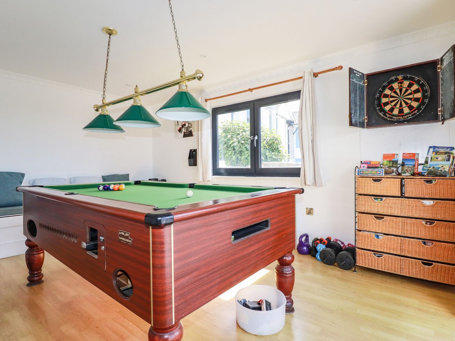 Een pooltafel met een groene viltkleed, een dartbord en een set halters.