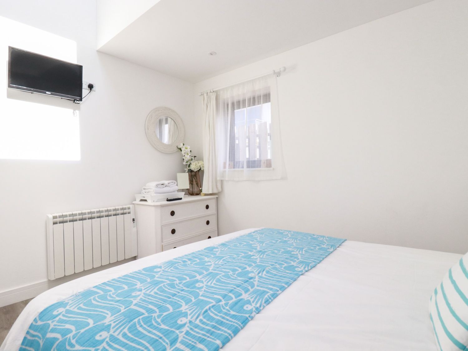 Un dormitorio con cama, cómoda, espejo, radiador y televisor montado en la pared.