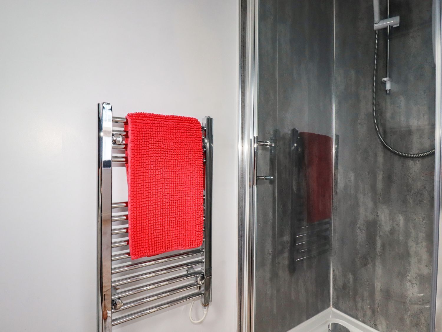 A bathroom with a chrome towel rack holding a red towel, a glass shower enclosure, and a white sink.