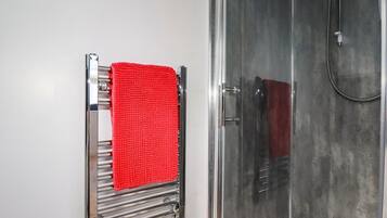 A bathroom with a chrome towel rack holding a red towel, a glass shower enclosure, and a white sink.