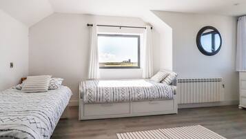 Un dormitorio con dos camas, una ventana con vistas, un radiador y un espejo circular en la pared.