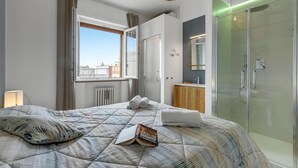 Un dormitorio moderno con una cama grande, una mesita de noche, una ventana con vistas, un vestidor y un box de ducha de vidrio.