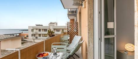 A balcony with a table set for breakfast, a chair, and a view of the sea.
