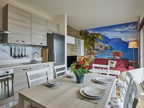 Une cuisine moderne avec un coin repas, une fresque représentant un paysage côtier et un canapé rouge.