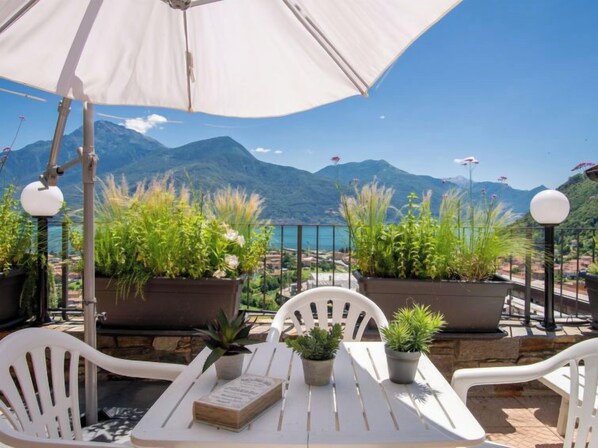 Une terrasse extérieure avec des chaises et des tables blanches, des plantes en pot et une vue sur les montagnes et un lac.