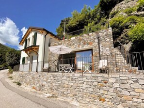 A stone building with a balcony, outdoor seating, and a mountain backdrop.