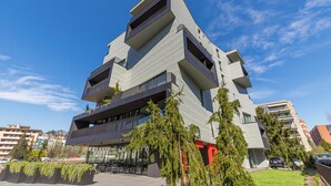 A modern multi-story building with balconies, a flat roof, and a clear sky.