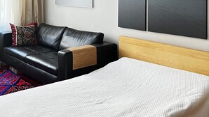 Una camera da letto moderna con un divano in pelle nera, un letto bianco e due grandi quadri astratti alle pareti.
