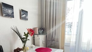 Un'area pranzo con un tavolo bianco, due sottopiatti rosa, un vaso con fiori e una sedia di legno.