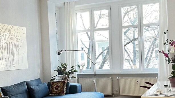 Un soggiorno moderno con un divano modulare blu, un tappeto colorato e decorato, e un'ampia finestra con vista su alberi spogli.