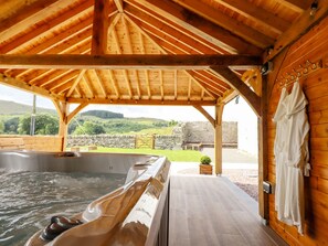 A wooden cabin with a hot tub and a stone wall in the background. - Plas Iolyn (Betws-Y-Coed)