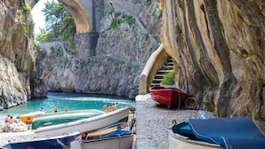 A stone bridge arching over a rocky shoreline with boats docked nearby.